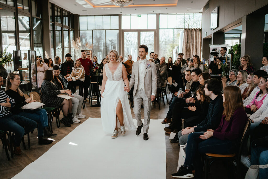 Modeshow waarbij koppel trouwjurk en trouwpak tentoonstelt tijdens trouwbeurs