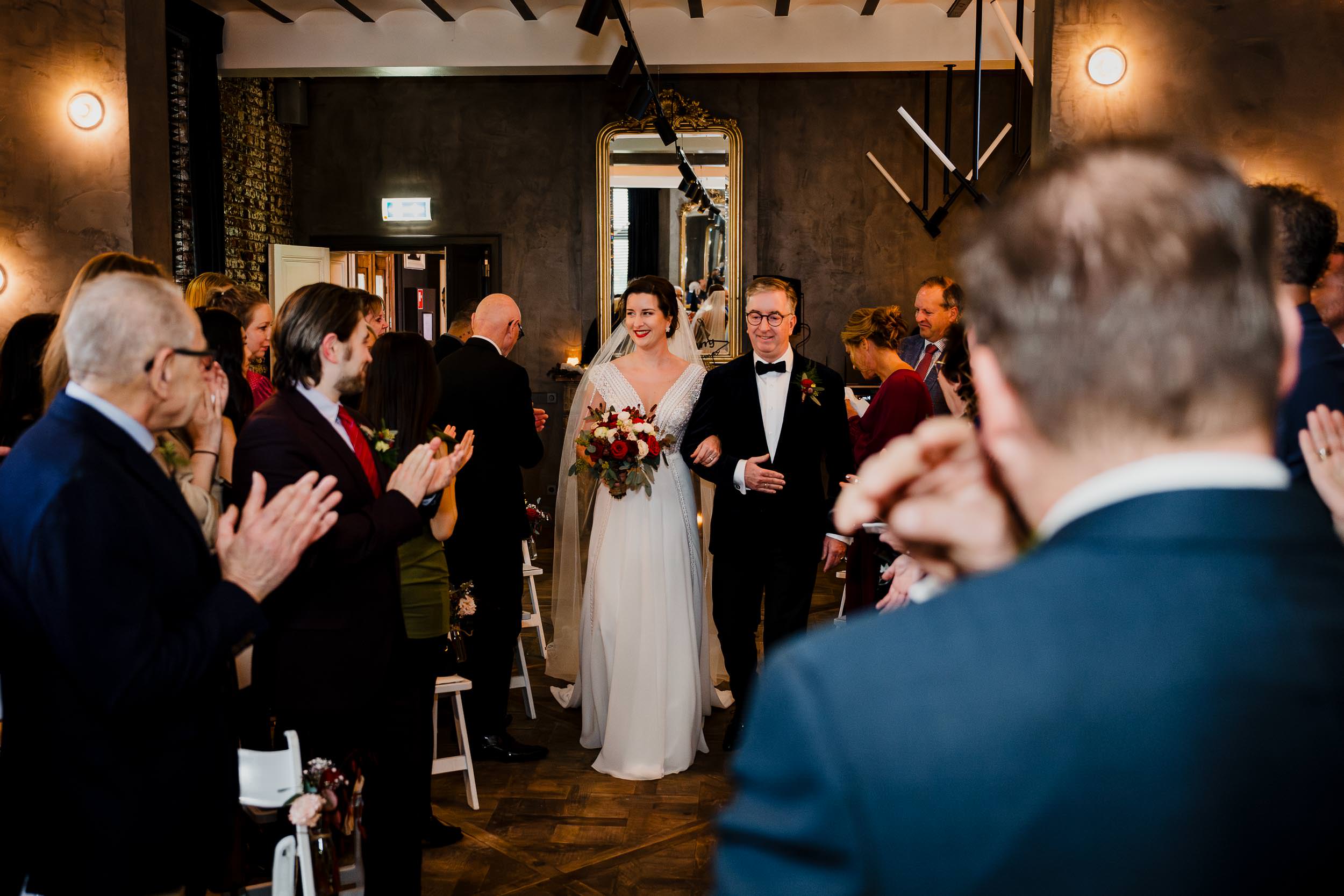 Bruid komt met vader en bruidsboeket aan lopen bij ceremonie
