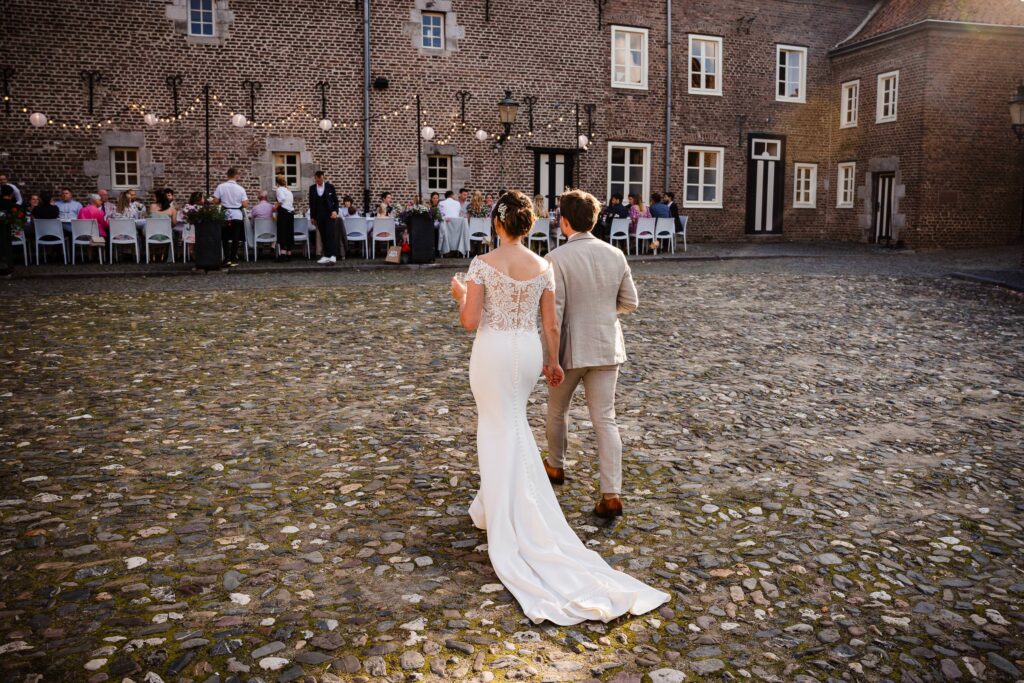 Bruidspaar loopt samen richting dinertafel op binnenplein met prikverlichting