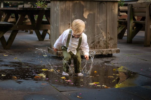 Kindje in bruidskleding stampt in een plas water