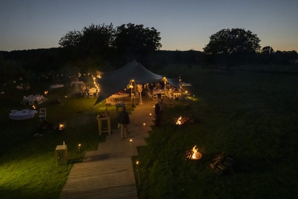 Bruiloft in weiland met looppad van vlonder naar de tent met vuurkorven en fakkels