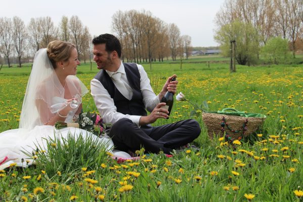 Bruidspaar zit in het gras tussen de bloemen