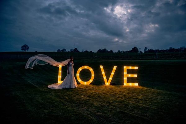 Lichtletters in het donker met bruid ervoor waarvan de sluier door de lucht zweeft